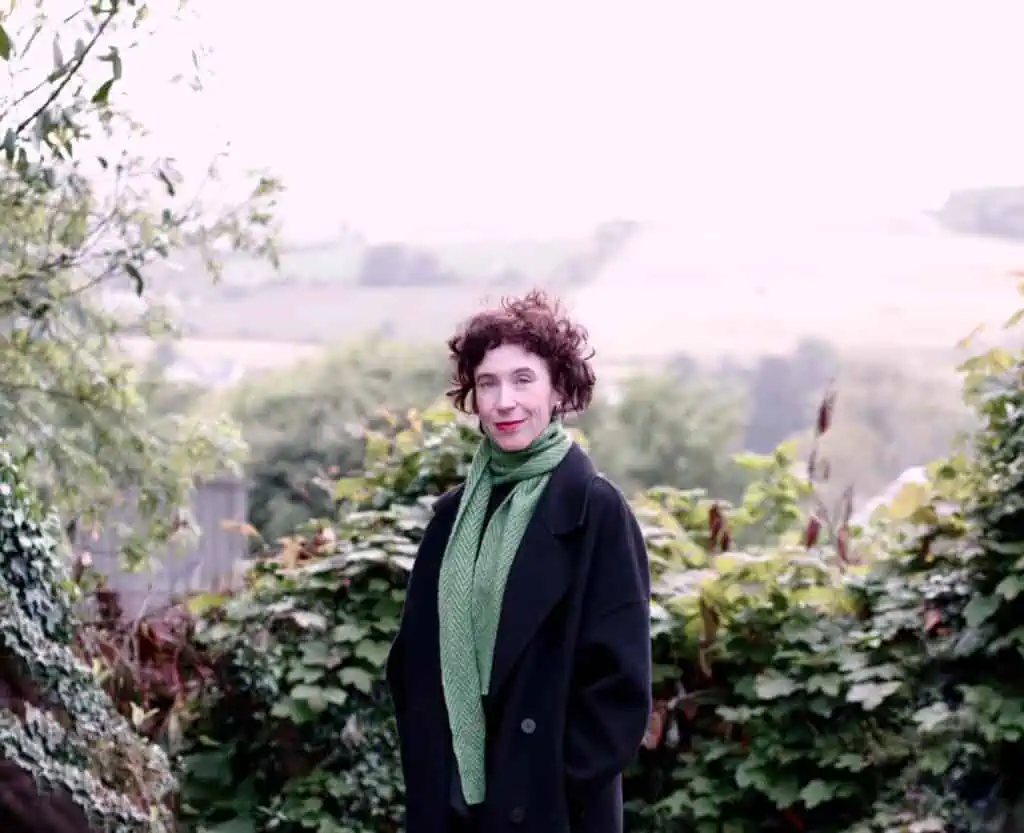 Niamh Campbell smiling in a black coat and green scarf with a countryside background