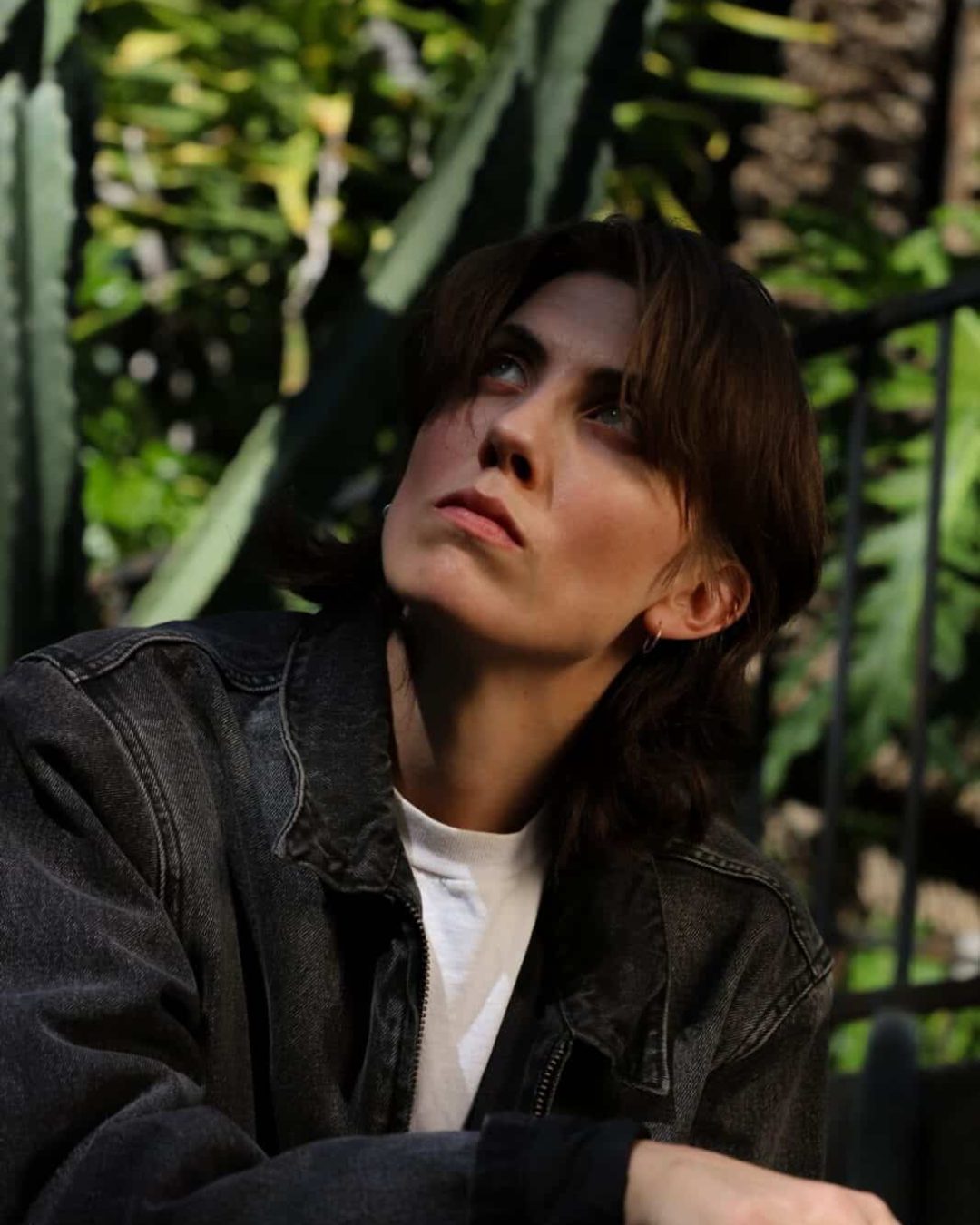 E.R. Fightmaster in a denim jacket looking up, with green cactus plants in the background