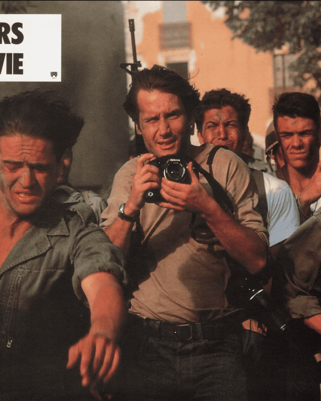A group of tense men, including a photographer with a camera, are being led by armed soldiers. The scene is chaotic and intense. The top left corner displays the text hors la vie in bold letters.