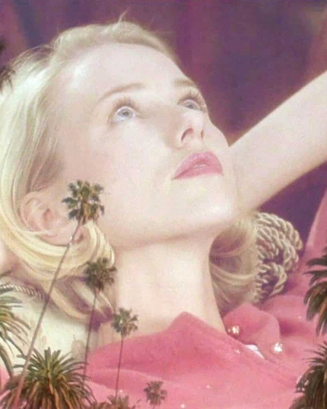 A blonde woman in a pink top reclines with her hands behind her head, gazing upward dreamily. Semi-transparent palm trees overlay the image, giving it a surreal effect reminiscent of a still from Mulholland Drive.